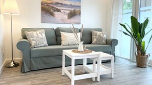 Un salón con un sofá gris, una mesita auxiliar blanca y una planta en maceta.