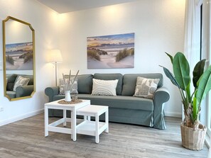 Una sala de estar con un sofá gris, mesas auxiliares blancas y dos cuadros de paisajes en la pared.