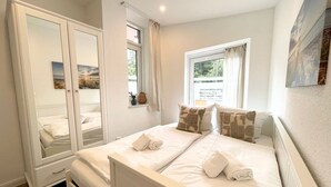 A bedroom with a bed, a wardrobe, a window with curtains, and a painting on the wall. - NB 3 - Stylish vacation apartment with private sauna and whirlpool bath - House (Cuxhaven)