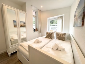 Une chambre à coucher avec un lit, une armoire, une fenêtre avec des rideaux et un tableau au mur.