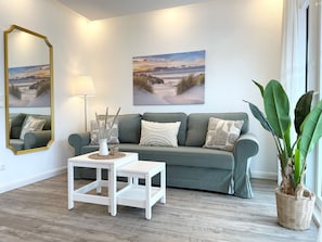 Un salon avec un canapé gris, des tables d’appoint blanches et deux tableaux représentant des paysages accrochés au mur.