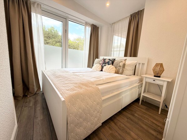 A bedroom with a bed, bedside table, and a view through the window.