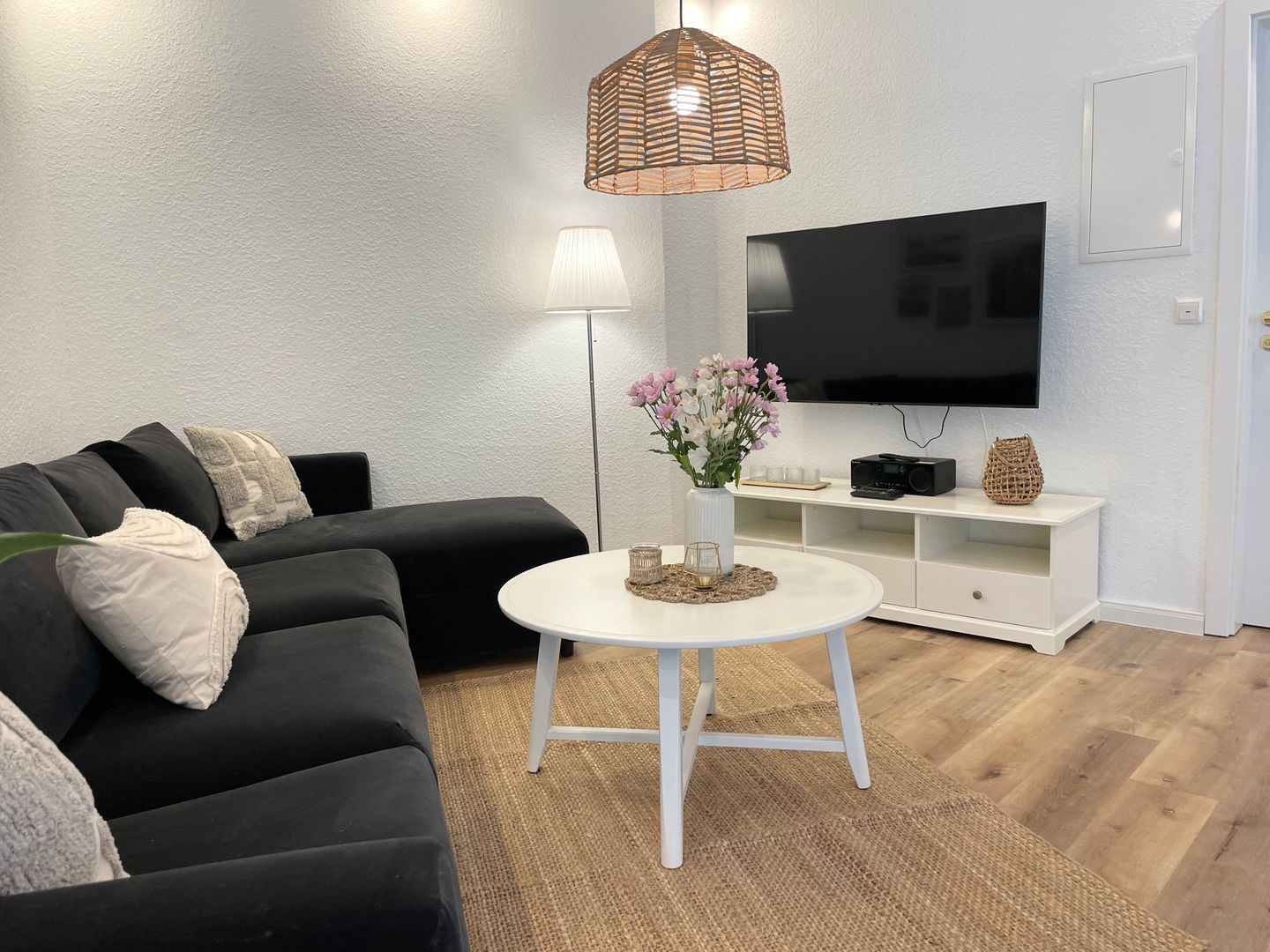 Un salon avec un canapé noir, une table basse blanche, un téléviseur et une lampe.