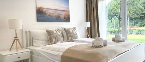 A bedroom with a bed, nightstands, a lamp, a painting, and a window with curtains.