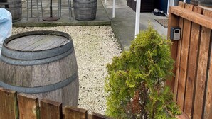 Un patio techado al aire libre con mesa y sillas de madera, una parrilla y un pequeño jardín con cerca de madera y una planta en maceta.