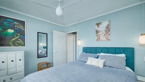 Un dormitorio con una cama, ventilador de techo, cómoda y obras de arte en las paredes.