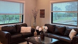 A living room with two dark leather sofas, a glass coffee table, and a ceiling fan. - Spring Branch Cottages "Texas Redbud" (Comal County)