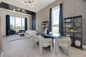A modern living room with a round dining table, white chairs, a sofa, and a bookshelf.