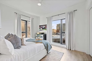 Un dormitorio moderno con una cama, un televisor y ventanas amplias.