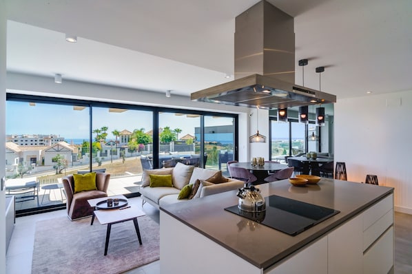A modern kitchen with a large island, a dining area with a table and chairs, and a seating area with a sofa and armchairs.