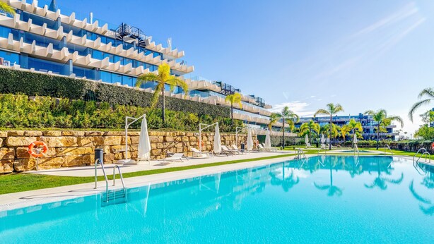 A swimming pool with lounge chairs, a lifebuoy, and a modern building with balconies. - Apartment 'Oasis 325' with Sea View, Wi-Fi and Air Conditioning (Estepona)