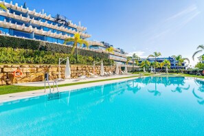 A swimming pool with lounge chairs, a lifebuoy, and a modern building with balconies.