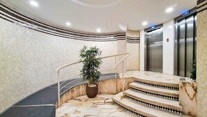 Un escalier en marbre menant à un ascenseur, entouré de murs recouverts de carreaux et agrémenté d’une plante en pot.