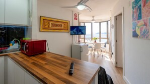 Une cuisine moderne avec un plan de travail en bois, un micro-ondes rouge, une télévision et un coin repas comprenant une table et des chaises.