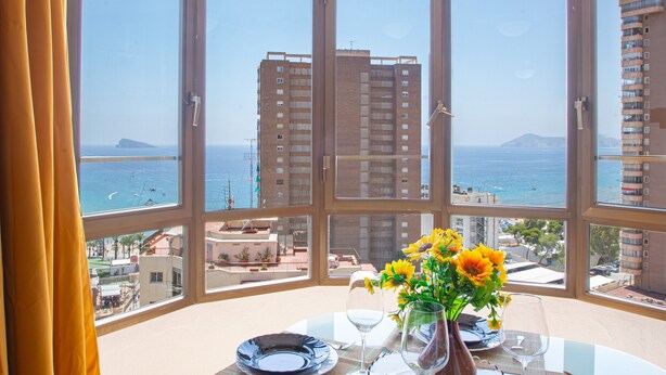 Une pièce dotée d’une grande baie vitrée, d’une table à manger dressée pour deux personnes et d’un vase rempli de tournesols.