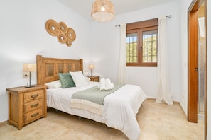 Ein Schlafzimmer mit einem hölzernen Bett, Nachttischen, einem fenster mit Vorhängen und einer Wandleuchte.