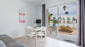 Ein modernes Wohnzimmer mit Balkon, weißen Möbeln und Blick auf einen Pool sowie Gebäude.