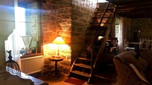 Ein rustikaler Innenraum mit einer Steinwand, einer Holztreppe, einem Tisch mit einer Lampe und einem Stuhl.