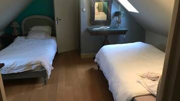 Una habitación pequeña y acogedora con dos camas, suelo de madera, un espejo y una mesita con una lámpara.