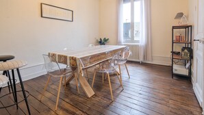 A dining area with a wooden table, clear chairs, a chandelier, and a radiator. - Miraflores – Spacious, Elegant Apartment in Central Périgueux with Wi-Fi (Périgueux)