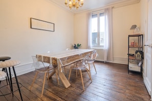 Un coin repas avec une table en bois, des chaises transparentes, un lustre et un radiateur.