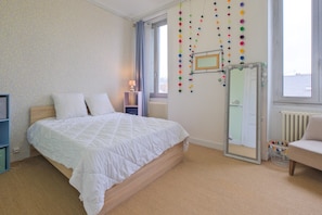 A bedroom with a bed, a window, a radiator, a mirror, and a chair.