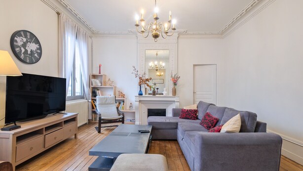 A living room with a television, sofa, ottoman, and fireplace. - Miraflores – Spacious, Elegant Apartment in Central Périgueux with Wi-Fi (Périgueux)