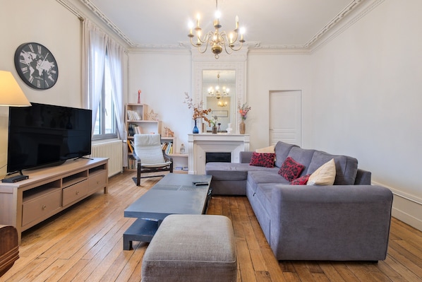 Un salon comprenant une télévision, un canapé, un pouf et une cheminée.