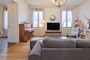 A living room with a sofa, a television, a piano, and a radiator.