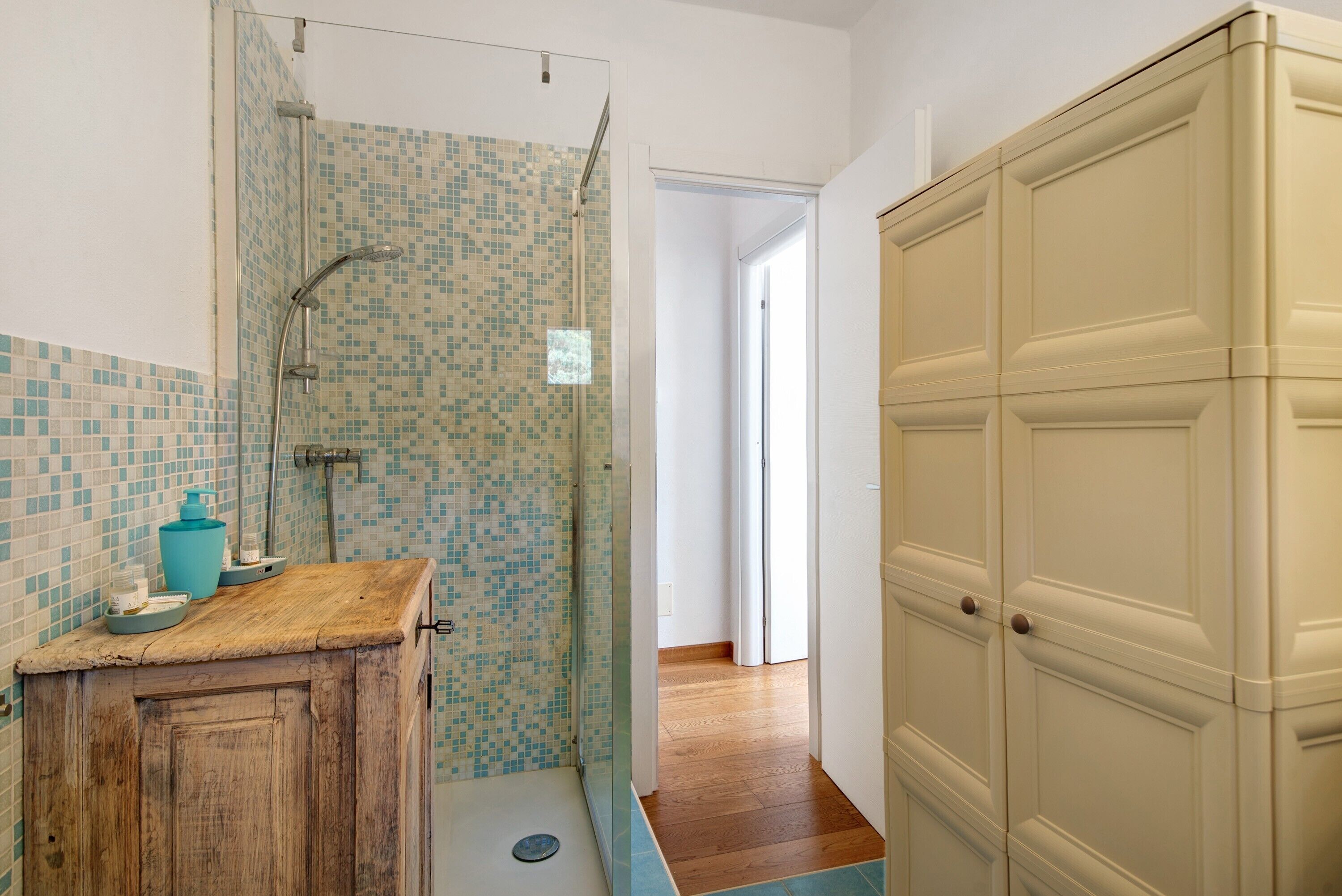 Un bagno con doccia, mobiletto in legno, pareti piastrellate e pavimento in legno.
