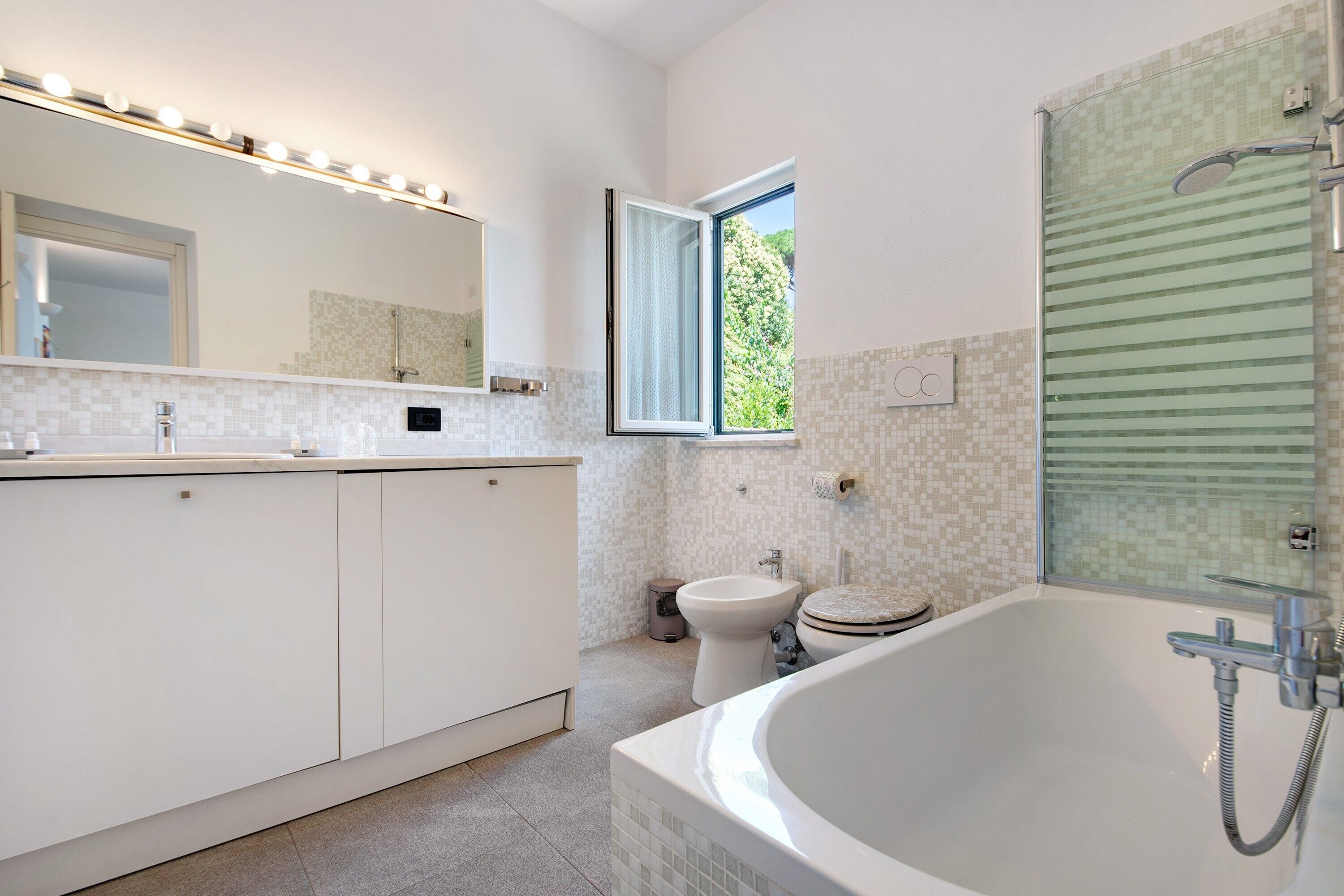Ein modernes Badezimmer mit einer großen Badewanne, einer Toilette, einem Bidet und einem Fenster.