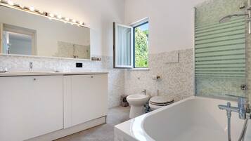 Ein modernes Badezimmer mit einer großen Badewanne, einer Toilette, einem Bidet und einem Fenster.
