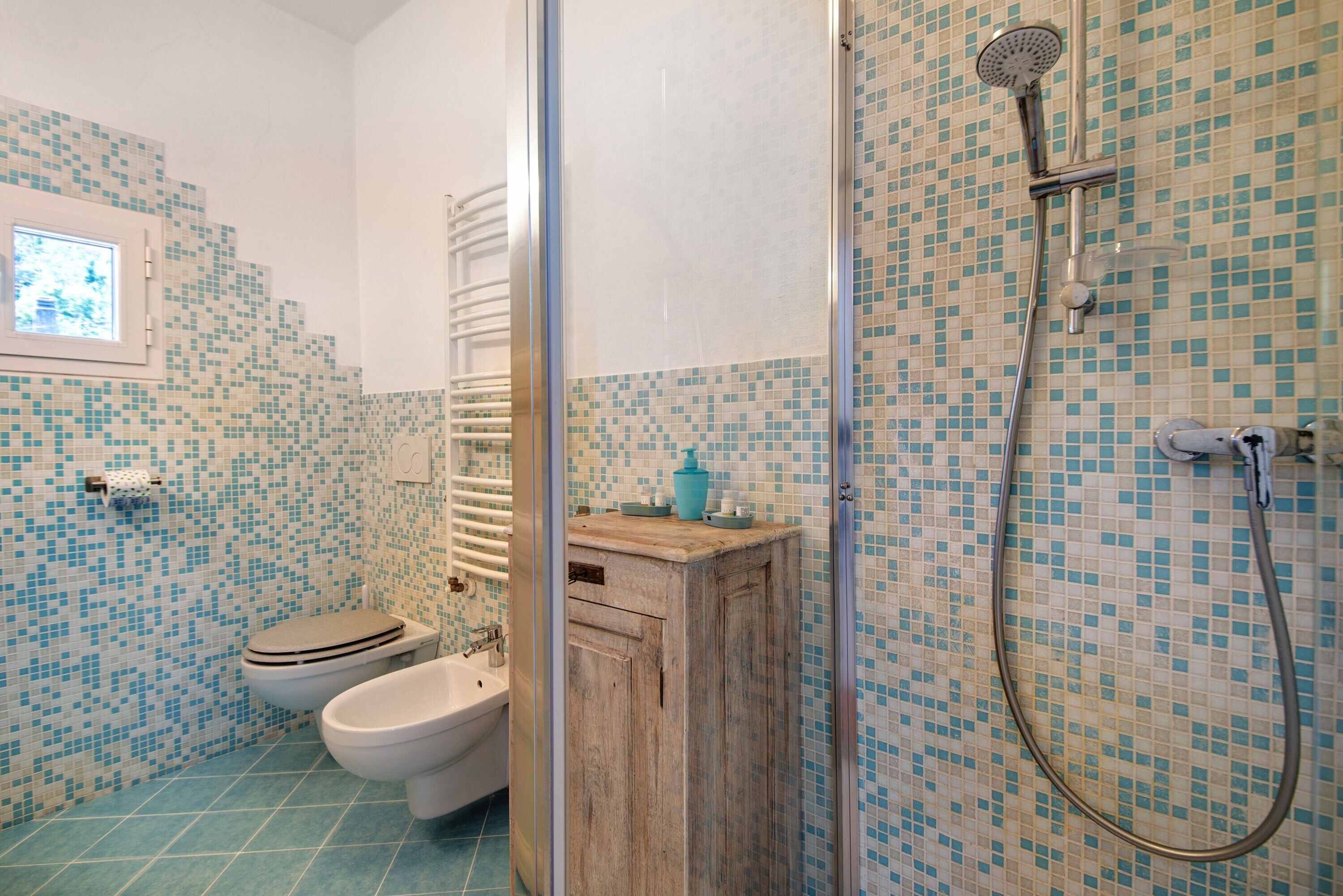 Ett badrum med toalett, bidé och dusch, med väggar och golv beklädda med mosaik.