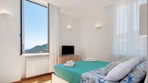 Ein Schlafzimmer mit Bett, Fernseher, Fenster mit Aussicht und Heizkörper.