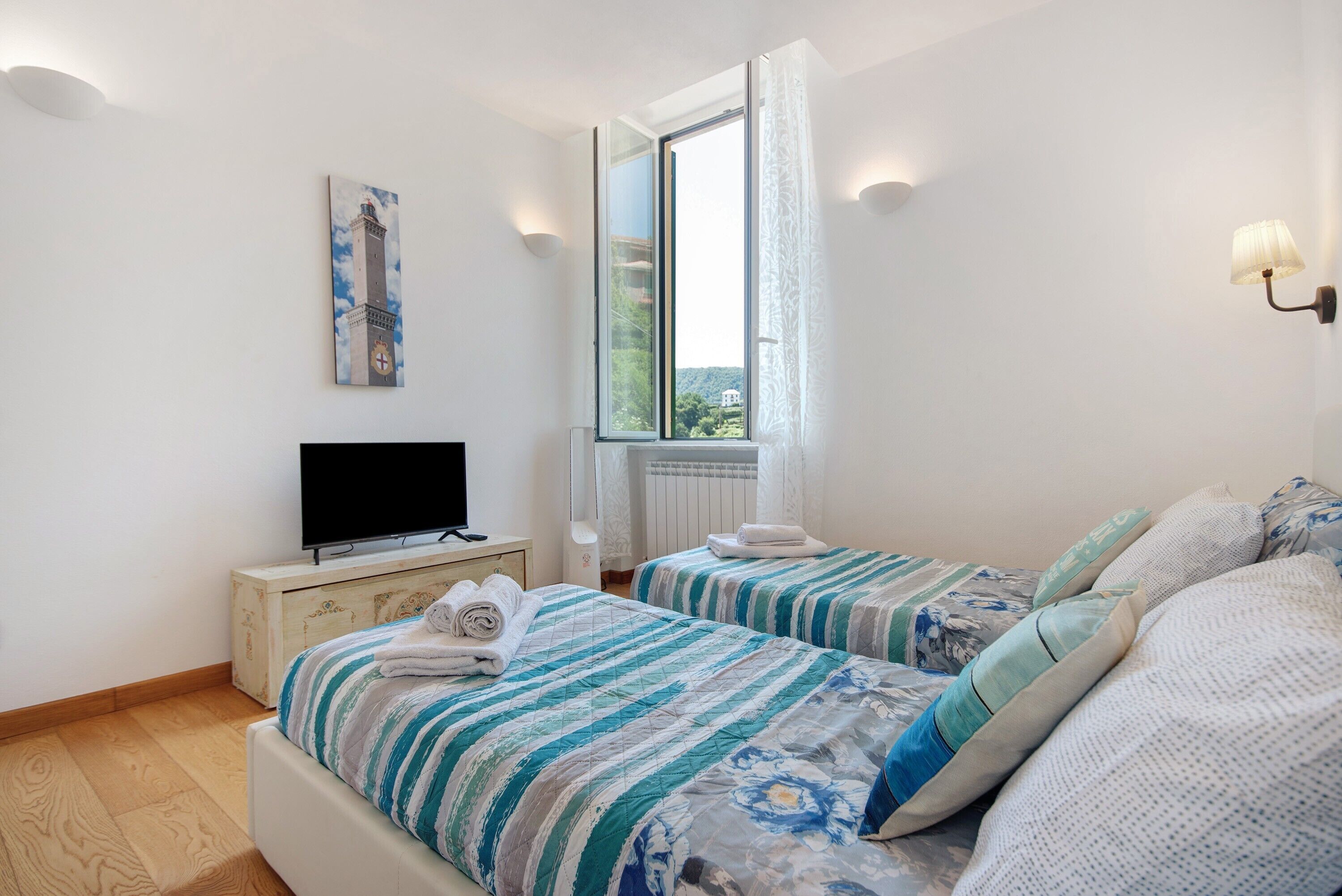 Una camera da letto con due letti, una televisione, un quadro e una finestra con tende.
