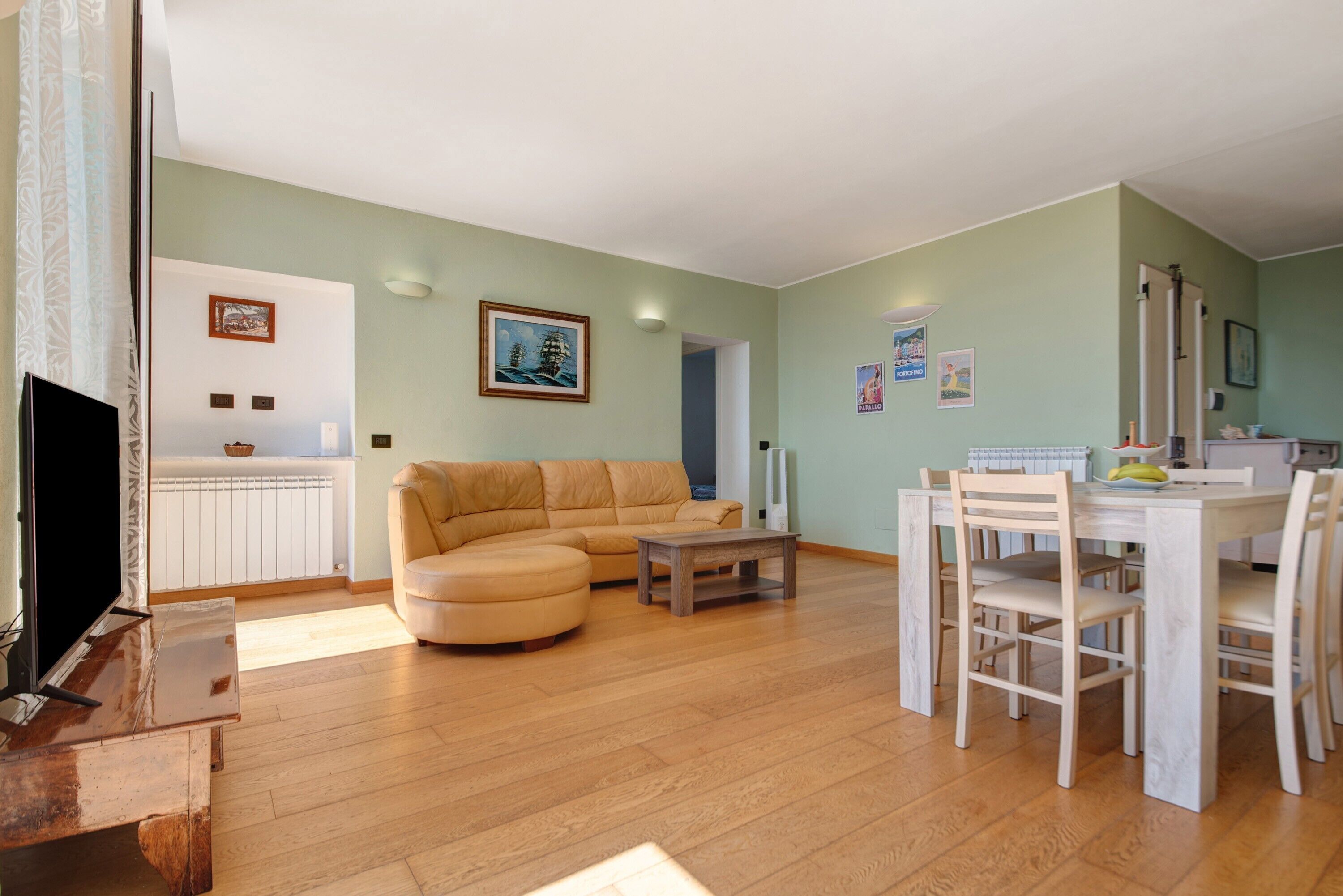 Een woonkamer met een bank, een eettafel met stoelen, een televisie en een keukenhoek.