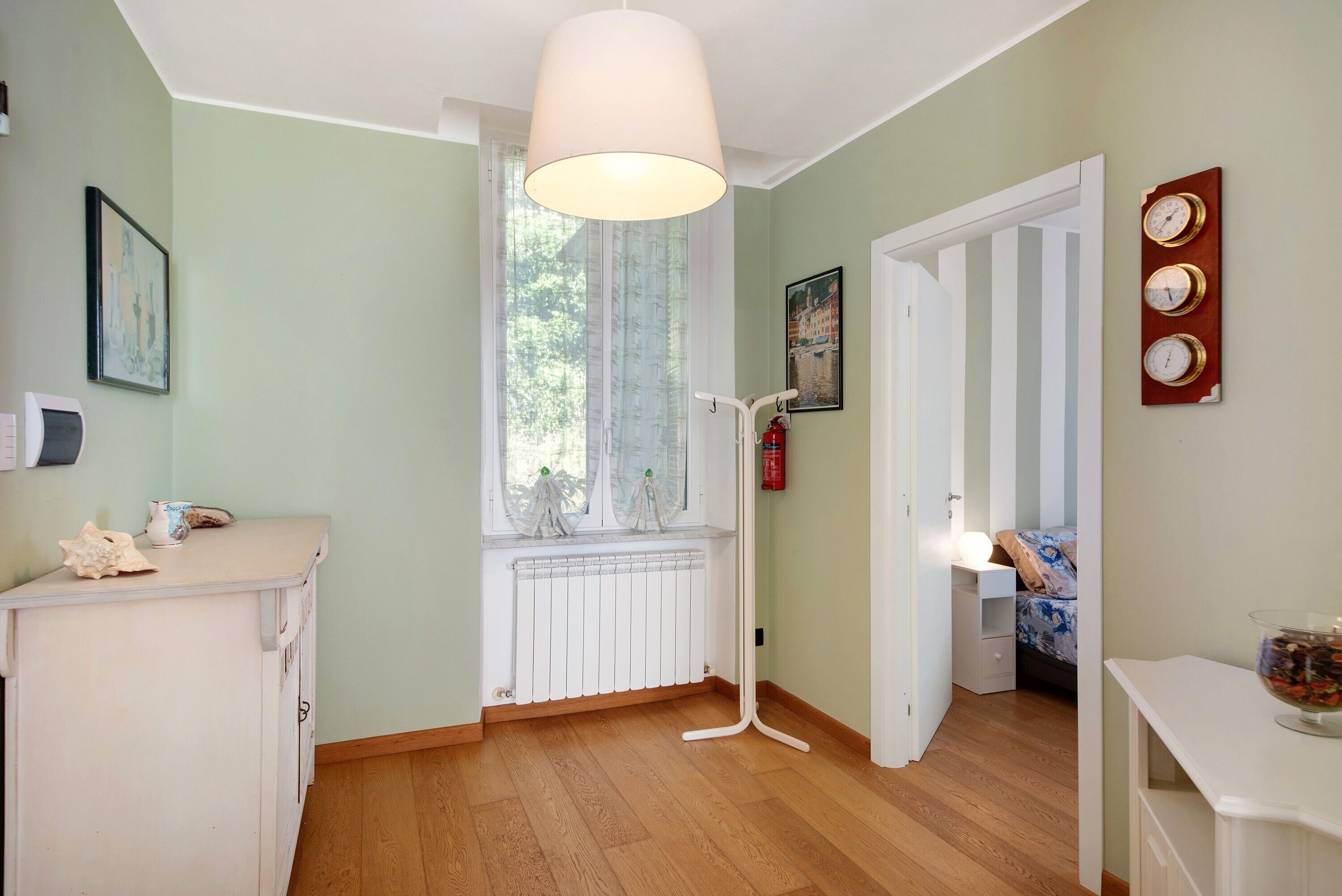 Une pièce avec un radiateur, une fenêtre avec des rideaux, une porte donnant sur une autre pièce et une horloge fixée au mur.