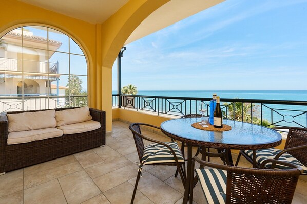 Ein Balkon mit einem Korbmöbel-Sofa, Korbstühlen, einem runden Tisch und Blick aufs Meer.
