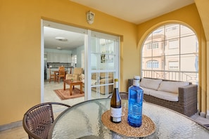 A glass table with a bottle and a water bottle, a wicker sofa, and a view through a glass door to a dining area.