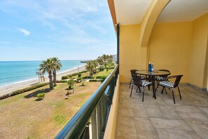 Ein Balkon mit Blick auf Strand und Meer, ein runder Tisch mit Stühlen und eine gelbe Wand.