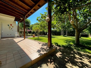A covered patio with a tiled floor, a white bench, and a potted plant.
