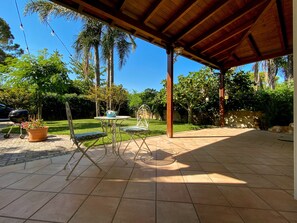 A covered patio with a tiled floor, a metal table with chairs, a grill, and potted plants. - Holiday Home 'Villa in the Ugento Natural Park' with Private Garden and Air Conditioning (Fontanelle)