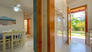 A room with a dining table, chairs, a ceiling fan, a wooden door, and a view of a garden.