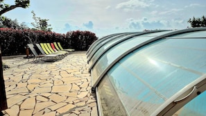 En swimmingpool med en buet glasindramning, fliseterrasse og liggestole.