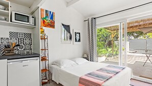 Un dormitorio con cama, microondas, lavamanos y ventana con vista a la vegetación.