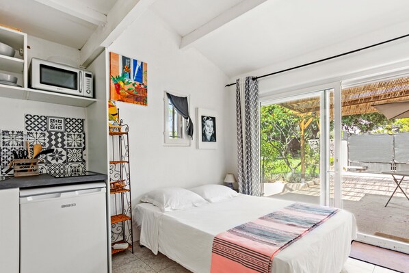 A bedroom with a bed, a microwave, a sink, and a window with a view of greenery.