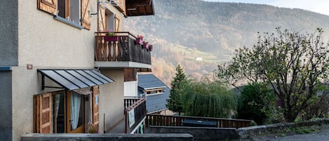 Um edifício de dois andares com varanda, antena parabólica e vista para uma paisagem montanhosa.