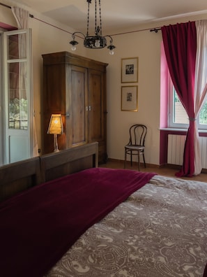 Une chambre à coucher avec un lit, une armoire en bois, une chaise, une lampe et une fenêtre avec des rideaux.