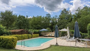 A backyard with a swimming pool, lounge chairs, and umbrellas.