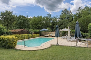 A backyard with a swimming pool, lounge chairs, and umbrellas.